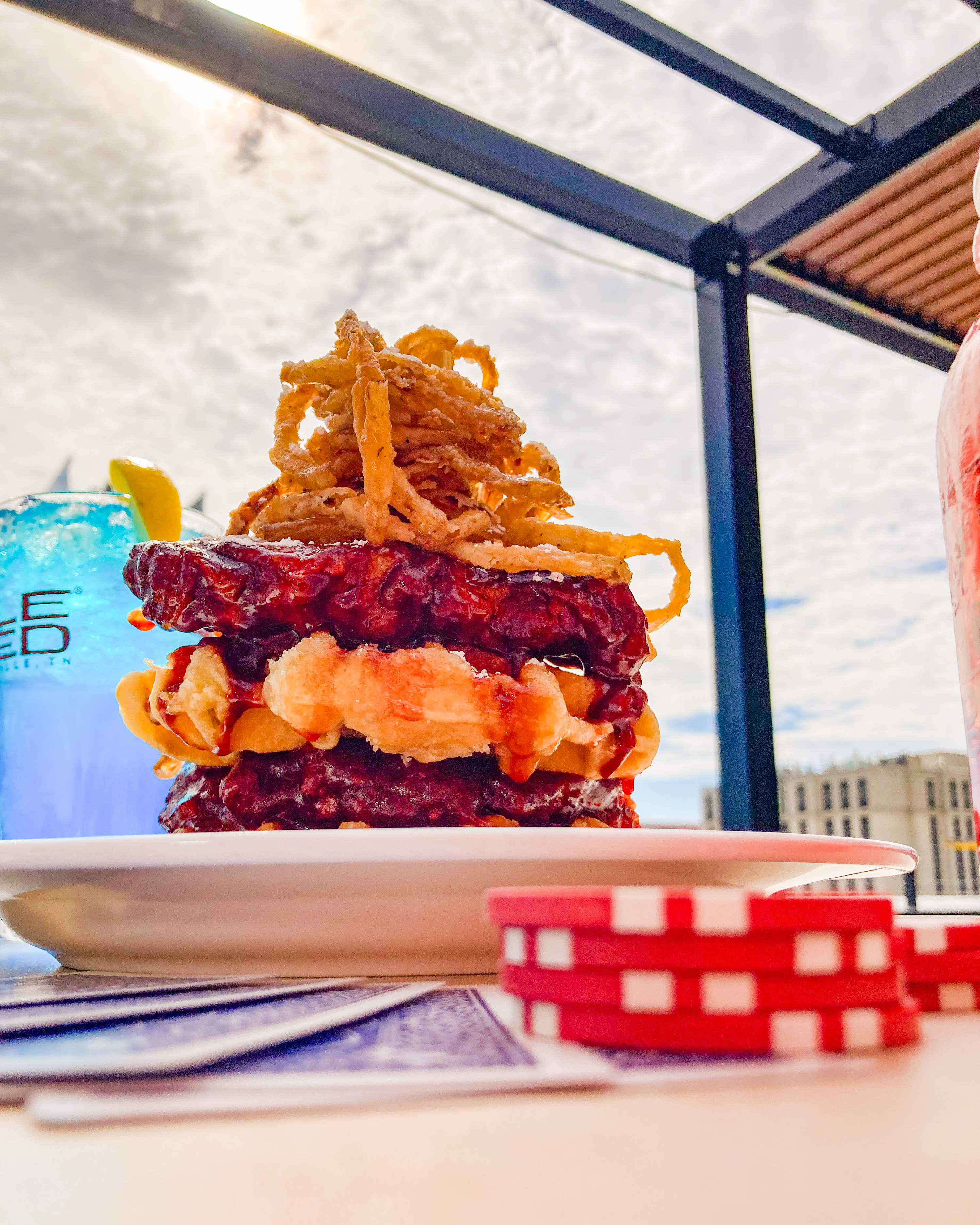 A stack of fried chicken coated in Honey Bee sauce, and a belgian waffle, topped with fried onion tangles. 