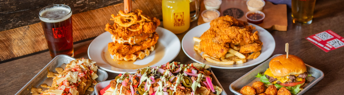 Table spread of Ole Red menu items, including nachos, bluetick burger and tots, fried green tomatoes, chicken and waffles, chicken and french fries, and an assortment of drinks.
